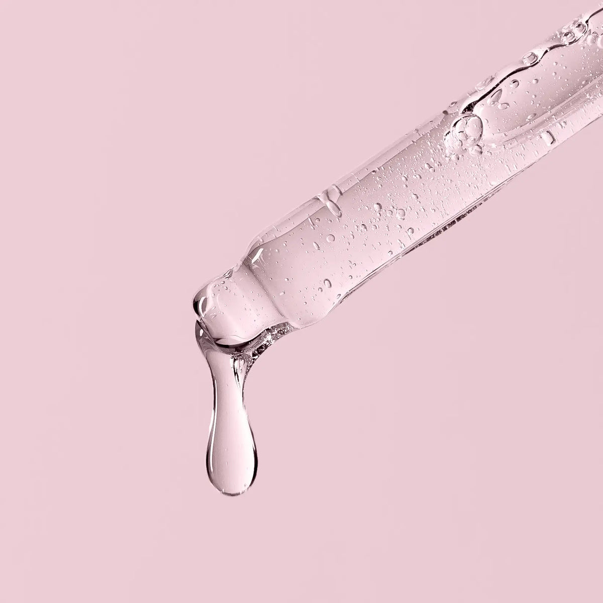 Pipette tropft klare Flüssigkeit auf rosafarbenem Hintergrund.