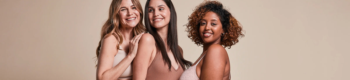 Three smiling women in fitted tops against a neutral background.