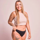 Frau trägt ein beigefarbenes Oberteil und schwarze Unterwäsche.
