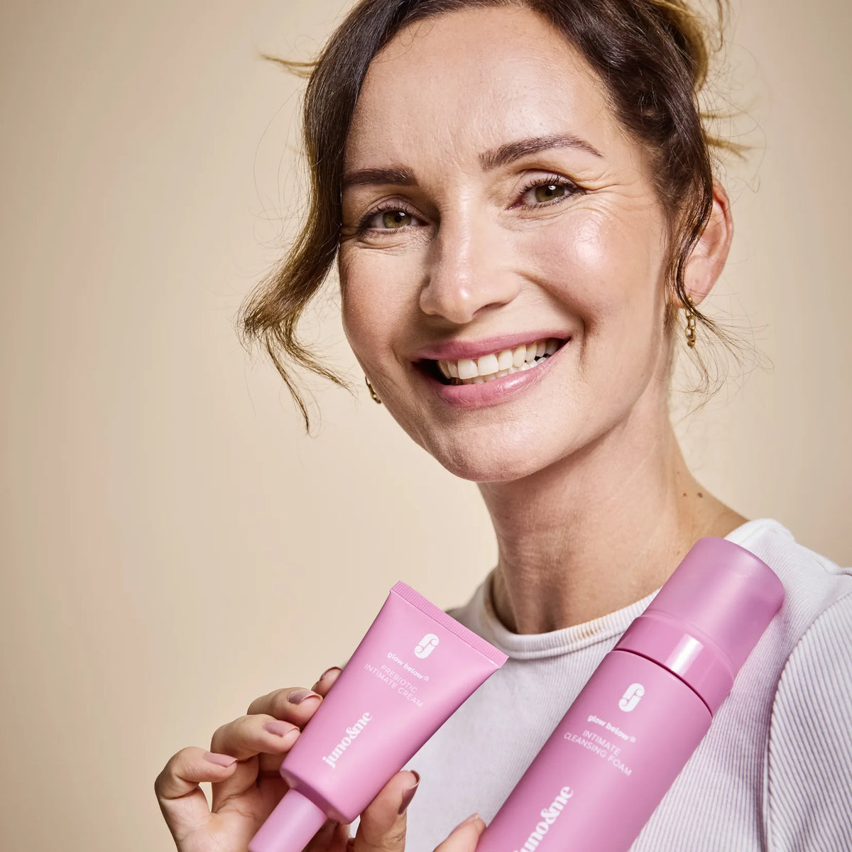 Lächelnde Frau hält Prebiotic Intimate Cream und Intimate Cleansing Foam von juno&me