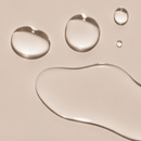 Clear drops of the Dry Touch Body Oil from the Touch Me Duo on a beige background, juno&me