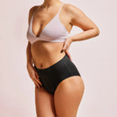 Frau trägt schwarze Periodenunterwäsche Seamless-High-Waist mit hellem BH.