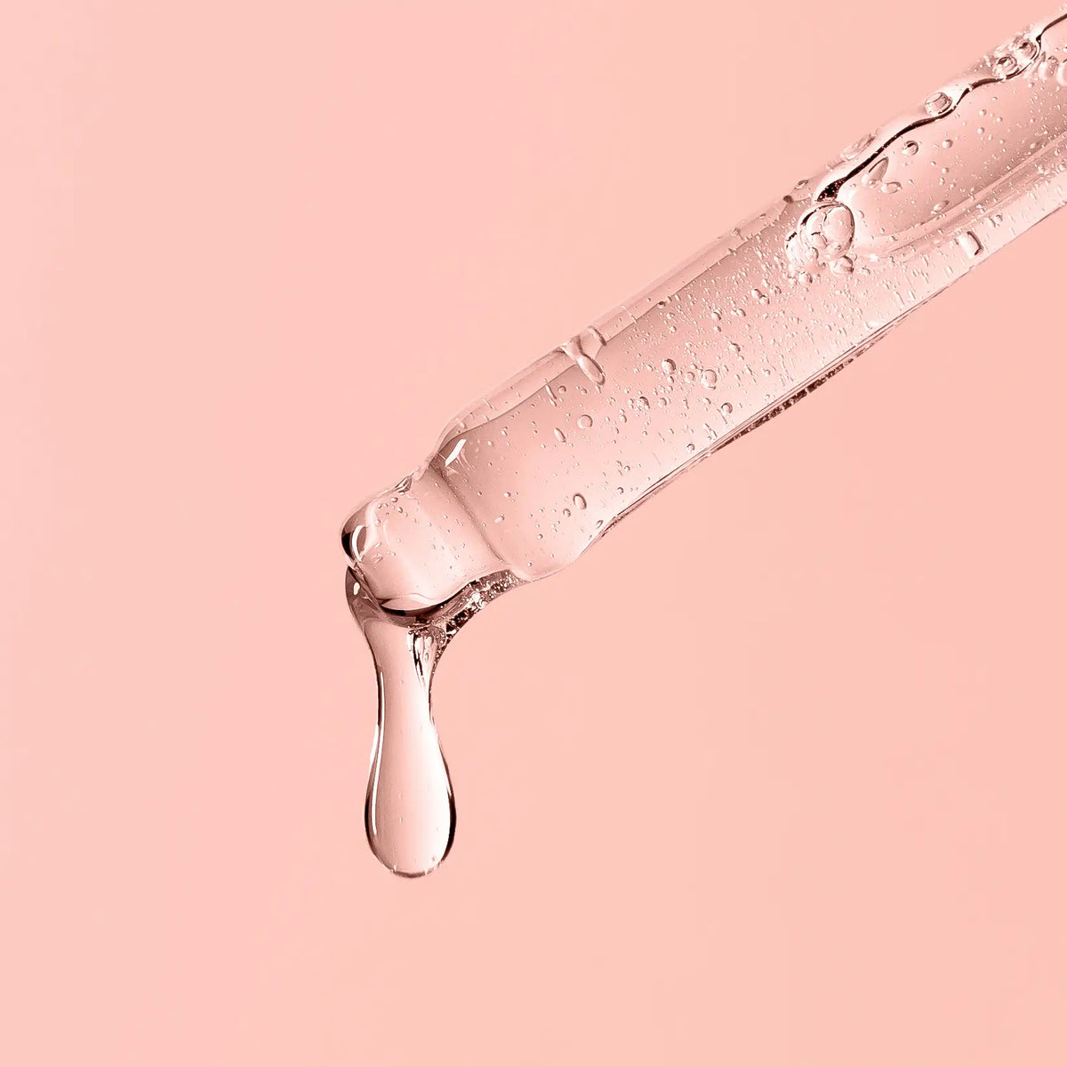 Pipette träufelt klare Flüssigkeit auf pastellfarbenem Hintergrund.
