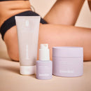 Drei Körperpflegeprodukte stehen vor einer sitzenden Frau im Hintergrund.
