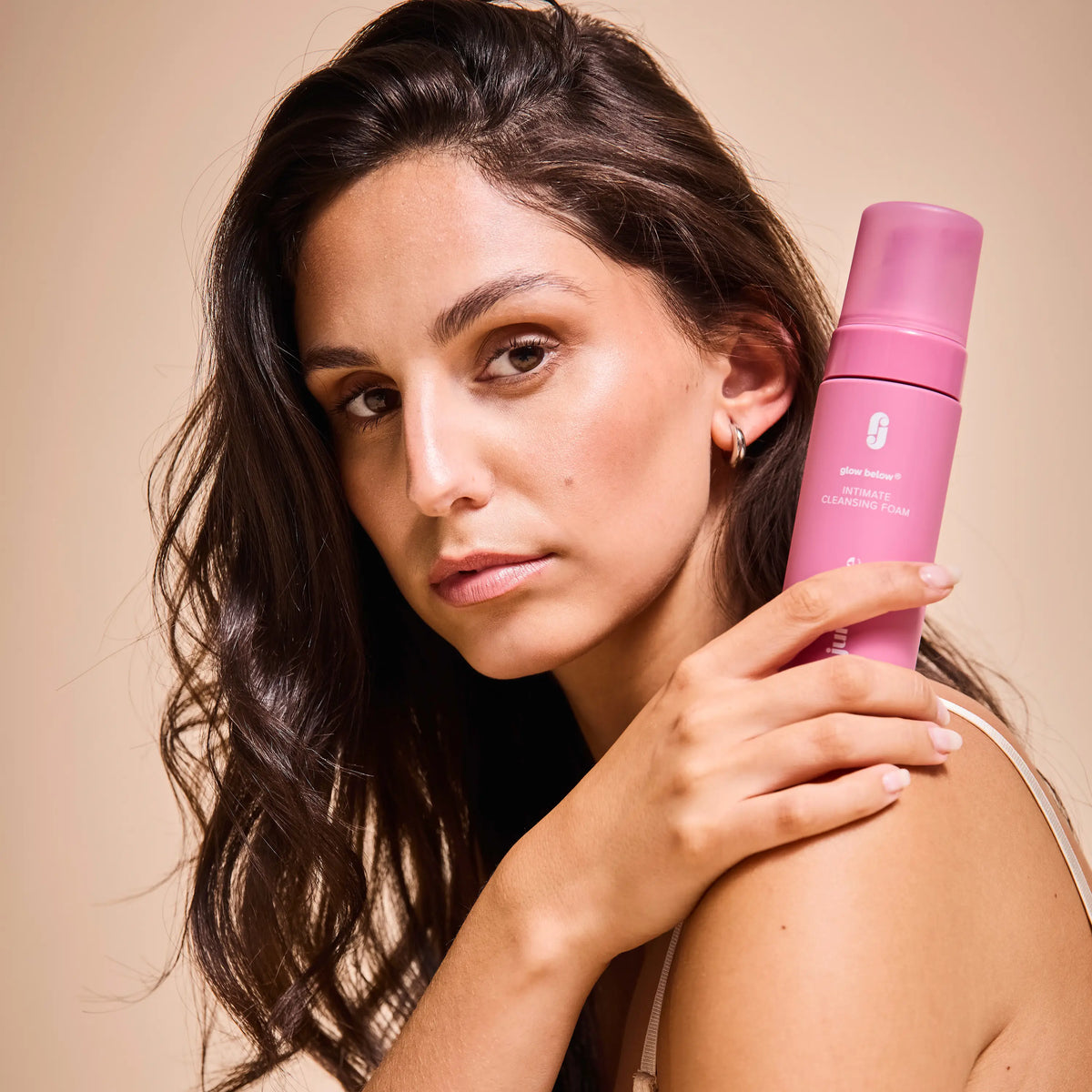 Woman holding the Intimate Cleansing Foam on her shoulder and looking at the camera