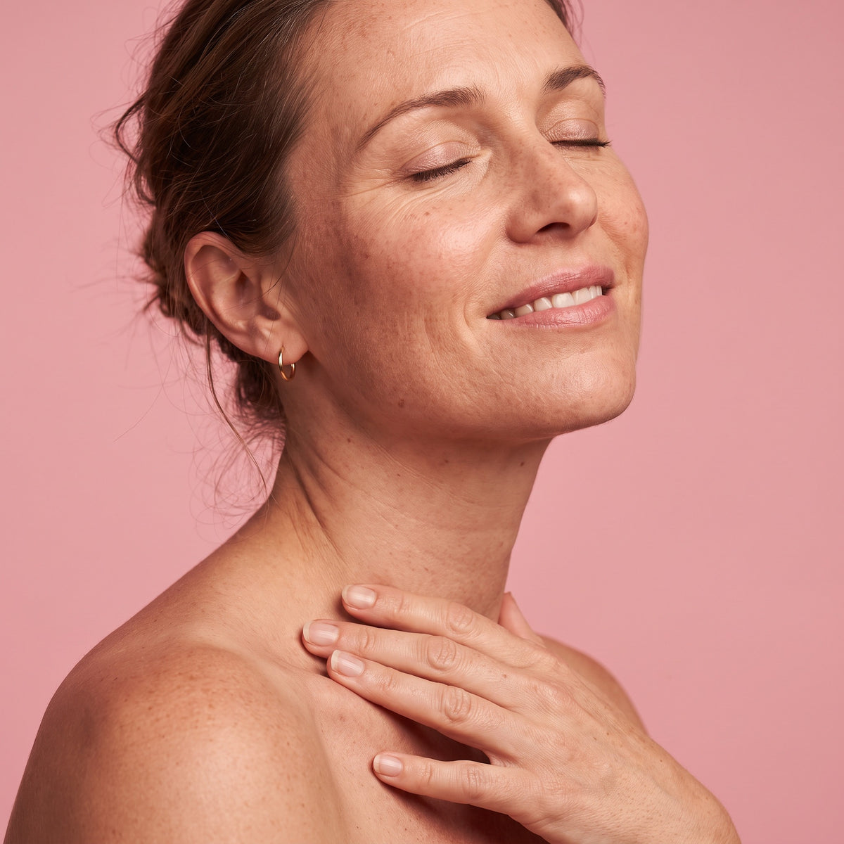 Woman with closed eyes and a relaxed smile, hand resting on her décolleté